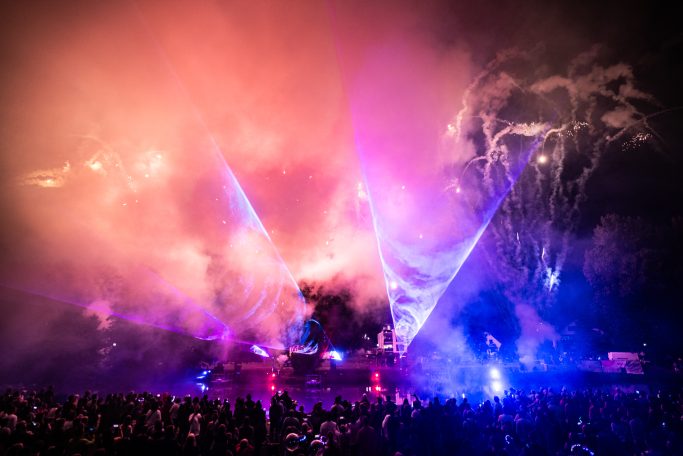 Buntes Lichtspiel mit Nebel und Laserstrahlen über einer Menschenmenge bei Nacht.